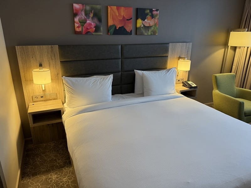 Hilton Garden Inn Wiener Neustadt – Doppelbett mit gepolstertem Kopfteil, weißer Bettwäsche und Blumenkunstwerk